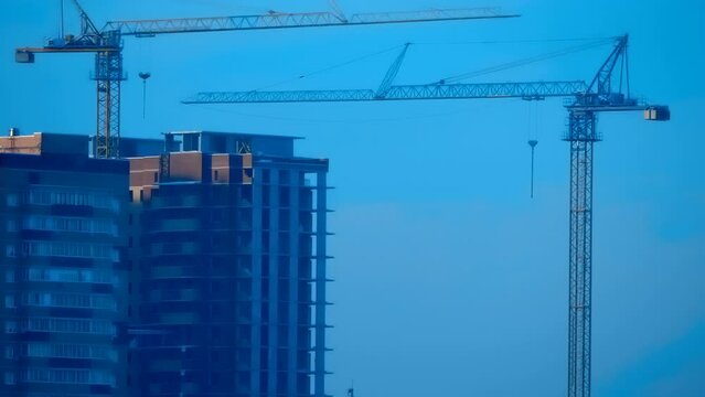 Two cranes next to a house under construction in a microdistrict of brick high-rise buildings in the middle of private houses covered with snow