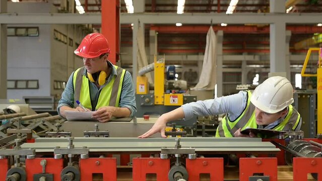 Two young engineers Testing and verifying the operation of the machines forming metal sheet tiles in the factory
