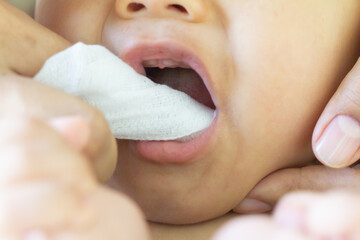 Mother cleans the teeth of a little boy, him to reduce pain from erupting , baby teethfingertip brush for children,  Clean cloth fter bathing at home, Asian family, hygiene. Zoom Selective focus