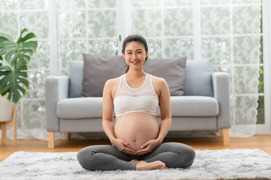 Happy Pregnant Asian Woman sitting on bed holding and stroking her big belly at home,Pregnancy of young woman enjoying with future life relax at home,Motherhood and Pregnant Concept,Soft focus