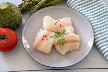 raw halibut fillet in a plate with fresh vegetables on a table - obrazy, fototapety, plakaty
