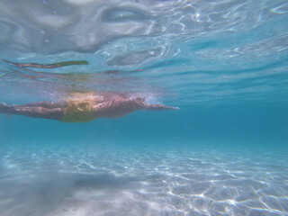 underwater scene of a man swimming crawl sltyle in a blue crystal clear watter beach. Concept of sport, holiday and travel.