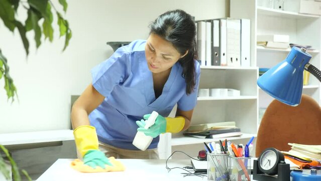 Woman cleans up desktop in office with a rag and cleaning products
