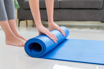 Yoga at home.  Young lifestyle woman rolling blue mat on floor after a workout in living room.