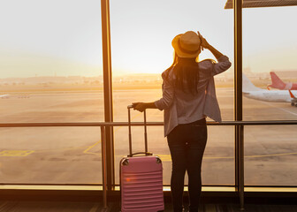 Happy explore travel concept with young tourist woman  holding the luggage and looking the airplane in the hall room with sunlight at the airport