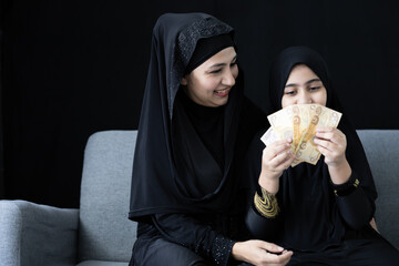 muslim woman or mother giving cash money to her daughter on black background