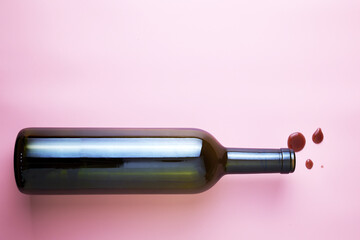 glass wine bottle and drops of red wine on a pink background copyspace