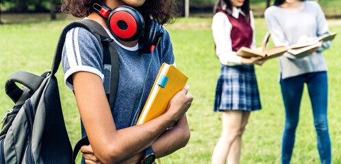 Smiling woman international student or teenager standing and holding book look at camera with group of student in park at university.Education and back to school concept