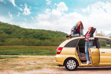 Travel banner. Caucasian mother and her teen daughter dreamy posing by a yellow car. The concept of freedom and travel on a car