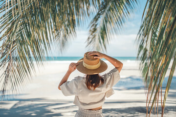 Summer beach vacation concept, Happy woman with hat relaxing at the seaside and looking away, in the summer against a backdrop of palm trees and sea beach. - Powered by Adobe