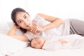 Obraz na płótnie Canvas Newborn baby sleeping, Beautiful Asian mother lying next to toddler with love and caring. mom asks not to make noise because the child is sleeping deeply.