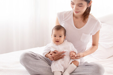 Fototapeta na wymiar Asian mother holding infant and looking baby with love and tender, mom play with toddler. Beautiful Asian women in white casual t-shirt and newborn in white cotton soft textile.