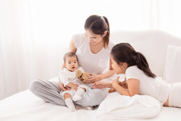 Older asian sister play and talk with newborn on bed in white room, Beautiful mother holding baby adorable and looking with love and caring. happy family concept.