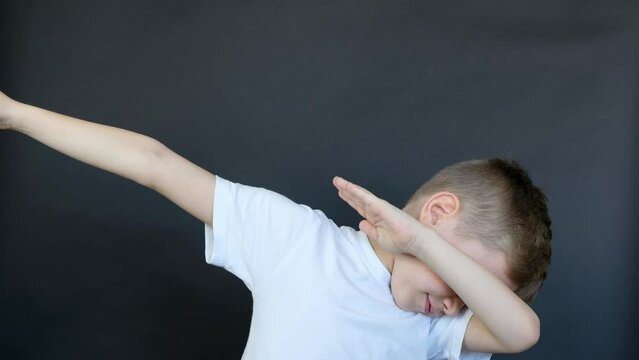 Cute blond caucasian boy in white t-shirt smiling doing dab hip hop dance hands move gesture , dark background