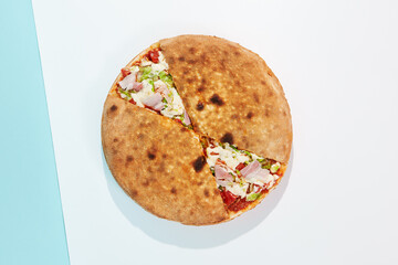 Italian closed pizza with cheese, bacon, tomato on coloured background. Calzone pizza with meat, cheese and vegetables in minimal style. American pizza delivery concept with color backdrop.