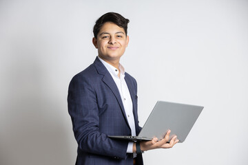 Young smiling Indian teenager boy wearing formal outfit holding laptop against white background. ...
