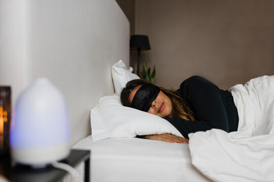 Young woman wearing eye mask sleeping on bed at home
