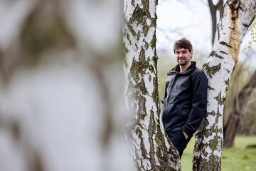 Smiling man with hand in pocket leaning on tree trunk