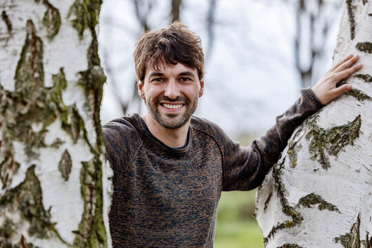 Happy man standing amidst tree trunks