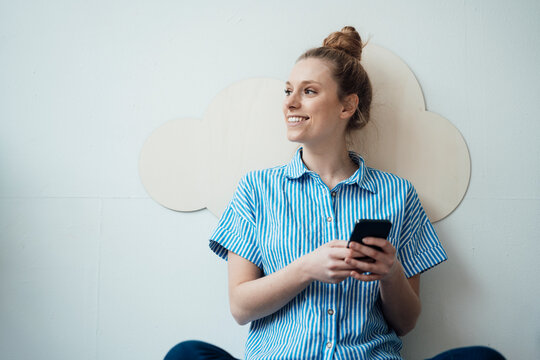Smiling businesswoman holding smart phone in front of wall