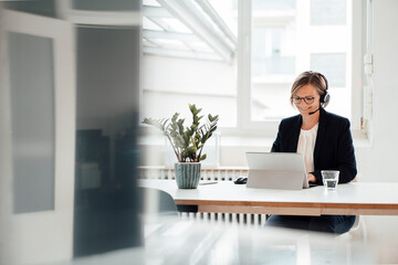 Happy businesswoman wearing headset talking on video call through tablet PC