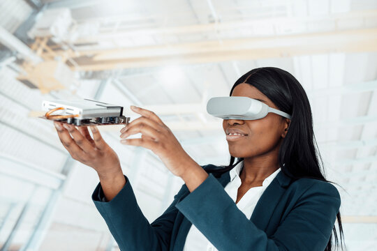 Smiling businesswoman wearing virtual reality simulator holding machine part in factory