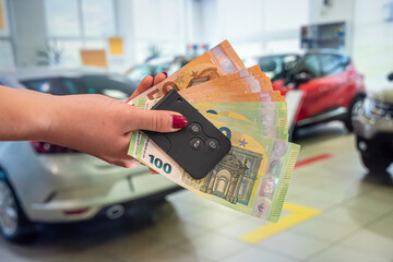 young well-groomed hands holding euro banknotes and car keys on the background of the car