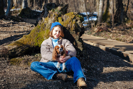 Smiling young woman with pet dog sitting in forest on sunny day
