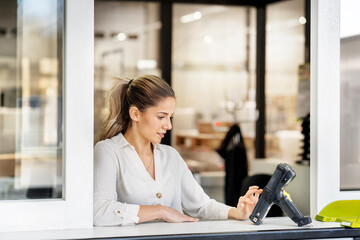 Young businesswoman using bar code scanner at window of factory