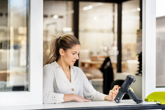 Young businesswoman using bar code scanner at window of factory