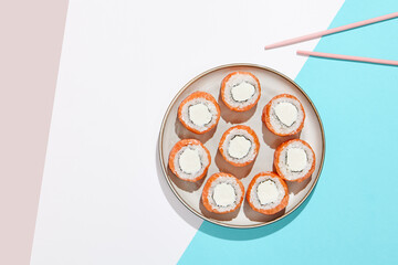 Philadelphia maki roll on ceramic plate with chopsticks. Salmon sushi roll with philadelphia cheese on coloured background. Japanese menu concept. Salmon sushi roll in modern style.