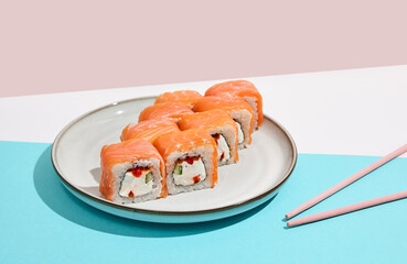 Salmon maki roll with red caviar on modern coloured background. Sushi roll with Philadelphia cheese, caviar inside, salmon outside. Moscow maki sushi in minimal style. Japanese menu concept.