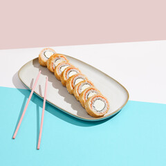 Baked Philadelphia Maki with salmon on ceramic plate. Hot tempura sushi with salmon and philadelphia cheese on coloured background. Japanese menu concept. Hot maki sushi in modern style.