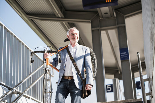 Smiling businessman carrying bicycle on shoulder walking at railroad station