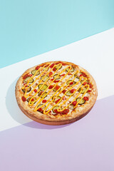 Italian pizza with chicken and pickled cucumber on coloured background. Cheese pizza with chicken in minimal style on purple and blue colours. American pizza delivery concept with color backdrop