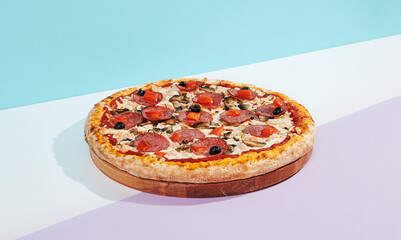 Italian pizza with salami, mushroom, black olives on coloured background. Meat pizza with salami and olives minimal style on blue and purple color. American pizza delivery concept with color backdrop