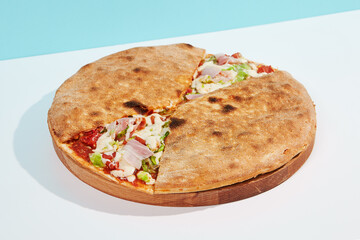 Italian closed pizza with cheese, bacon, tomato on coloured background. Calzone pizza with meat, cheese and vegetables in minimal style. American pizza delivery concept with color backdrop.