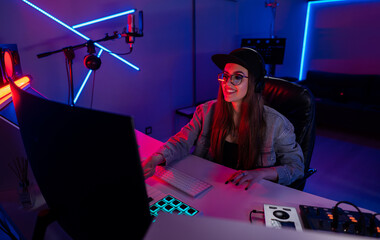 Beautiful caucasian girl in stylish clothes works in a recording studio with neon light in a cap...