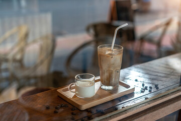 A tall glass of iced latte coffee with milk cream on a wooden counter bar over a cafe glass window reflex at a Cafe coffee shop. Cold brew refreshment summer drink with copy space Selective focus