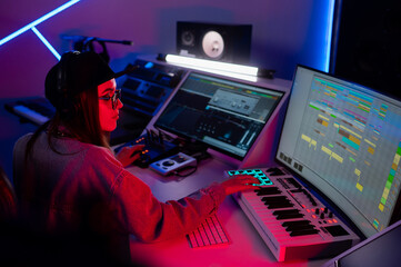 Beautiful caucasian girl in stylish clothes works in a recording studio with neon light in a cap and glasses - obrazy, fototapety, plakaty