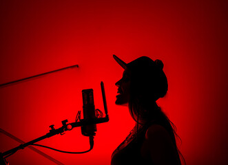 Silhouette of a beautiful girl with a red light singing into a studio microphone in a recording studio