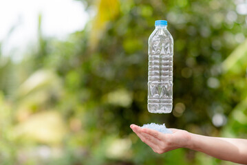 A woman's hand is holding plastic flakes and a plastic bottle to be recycled and feels the...