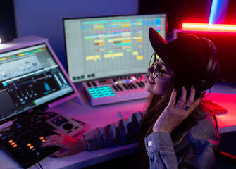 Beautiful caucasian girl in stylish clothes works in a recording studio with neon light in a cap...