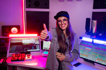 Beautiful stylish girl sound engineer in a recording studio with neon lights in a cap and glasses