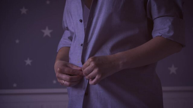 Pregnant woman opens her shirt and showing her belly, close-up. Unrecognized pregnant female unbuttons shirt to expsose belly at home, night shooting. Maternity concept.