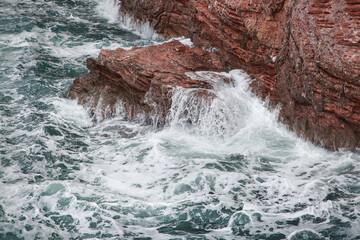 Sea waves break on red rocks and flow down in jets, natural background.