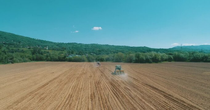 Drone aerial shot of a farmer in tractor seeding, sowing agricultural crops at field
