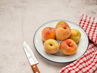 Fresh peaches fruits on a white dish, knife, and cloth on a table