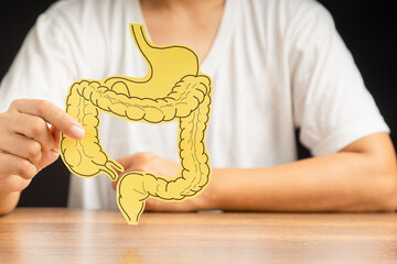 Hand holding a large intestine shape made from paper while sitting over a black background