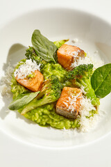 Gourmet food - green risotto with broccoli and salmon on white background. Italian lunch with risotto and sliced grilled salmon. Contemporary dish for restaurant menu. Hard shadow in sunshine day.